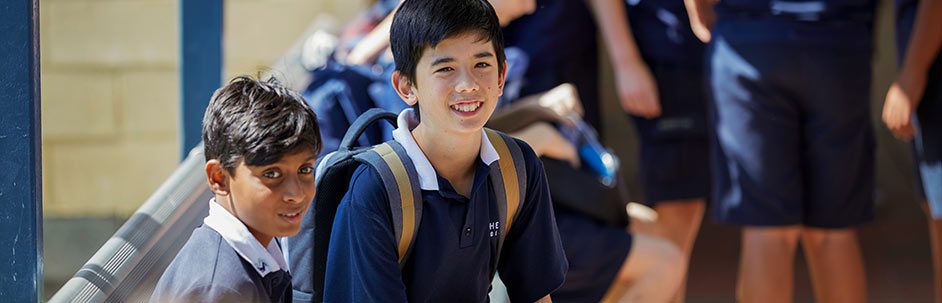 Two male students talking and smiling while sitting with backpacks on a bench outside