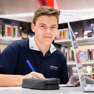 Male student in the library holding a pen and smiling at the camera